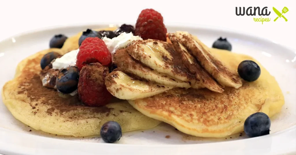 Stack of fluffy pancakes topped with syrup and fresh fruit.