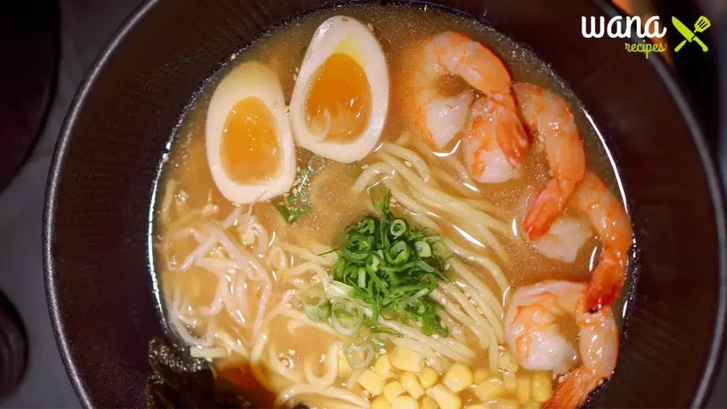 A delicious bowl of breakfast ramen with noodles, eggs, bacon, and fresh scallions, served in a white bowl.