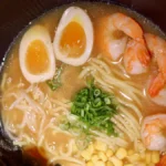 A delicious bowl of breakfast ramen with noodles, eggs, bacon, and fresh scallions, served in a white bowl.