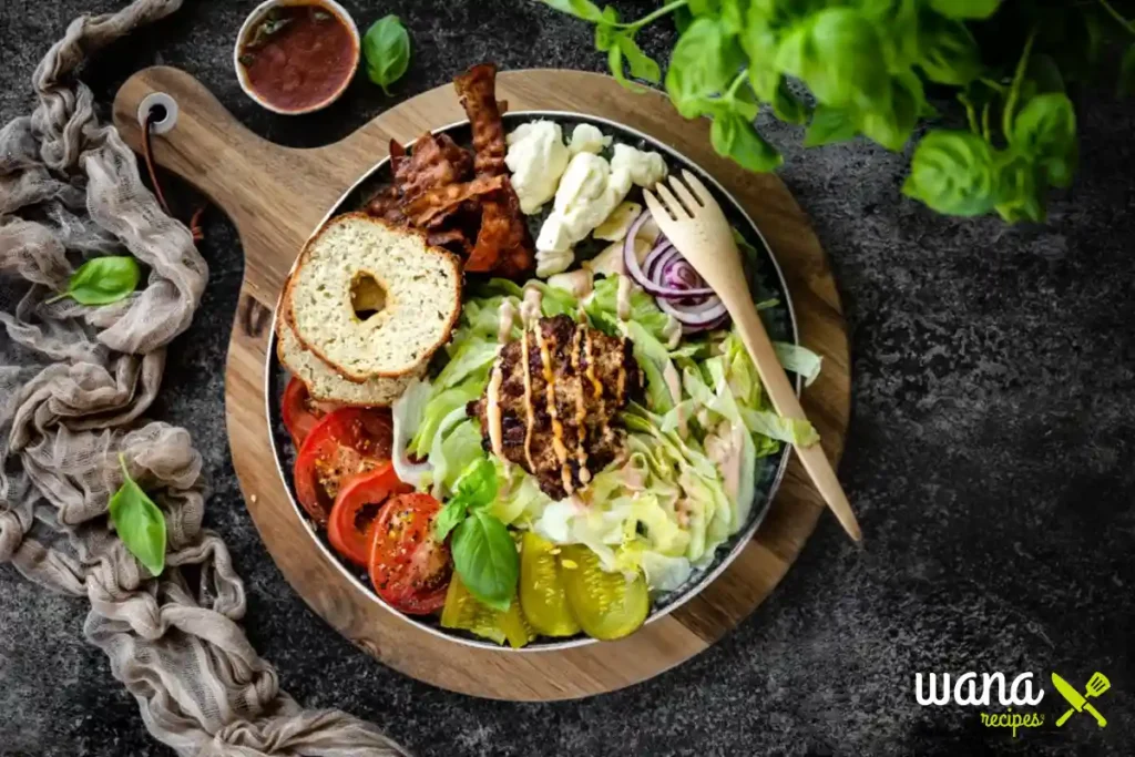 Low-carb burger bowl with lettuce, grilled beef patty, bacon, pickles, tomatoes, onions, and special sauce, served on a wooden board.