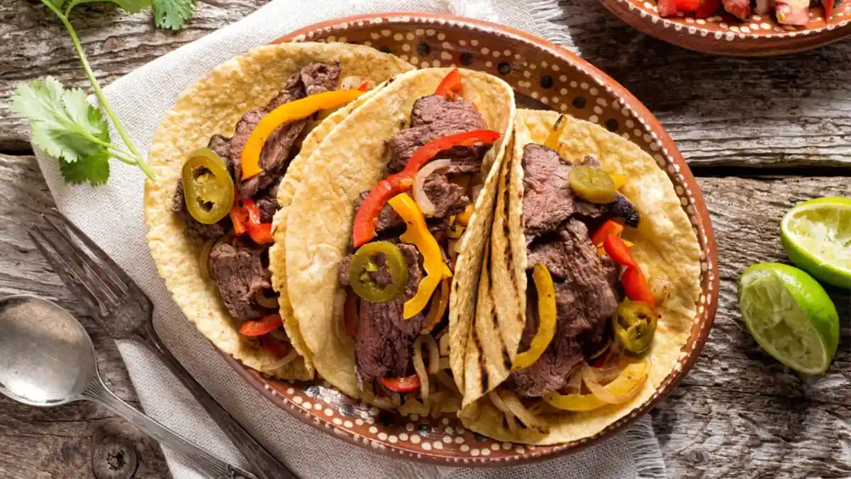 Delicious grilled steak elote tacos served on a plate with fresh lime wedges, cilantro, and cotija cheese, showcasing bold Mexican flavors.