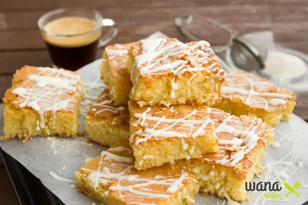 Slices of kefir sheet cake drizzled with white icing and stacked on parchment paper.