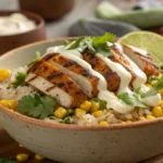 A close-up of a Street Corn Chicken Rice Bowl with grilled chicken, corn, rice, creamy lime sauce, and cilantro garnish.