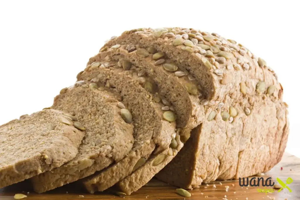 Whole wheat sunflower pumkin seed bread, fully sliced, revealing its soft, fluffy texture and crunchy seed topping, placed on a wooden surface.